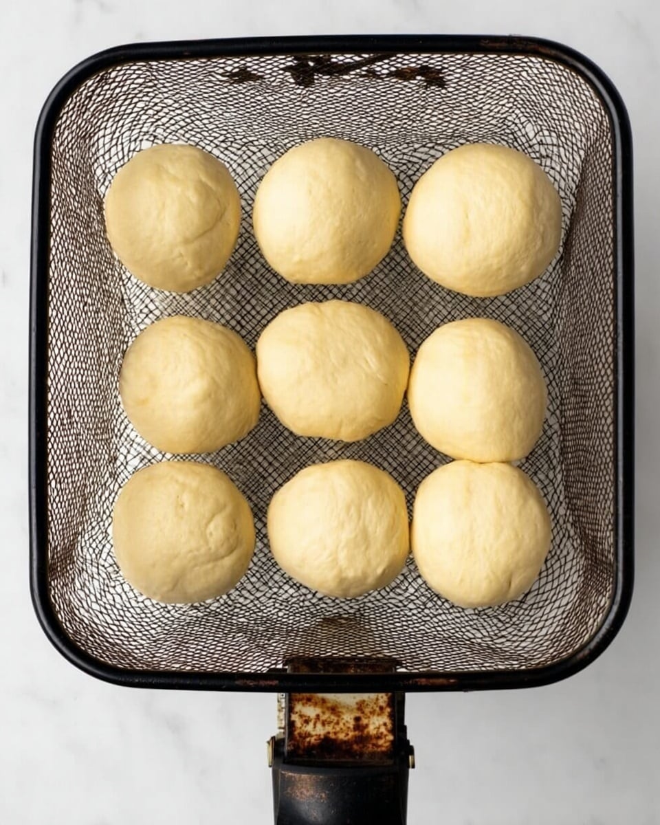 A white square basket with a black frame holds eight pale dough balls evenly spaced inside. The dough balls are round and smooth with a soft yellow tint. The basket has a mesh bottom showing a white marbled surface beneath. The handle is black with a rusted metal joint connecting it to the basket. photo taken with an iphone --ar 4:5 --v 7