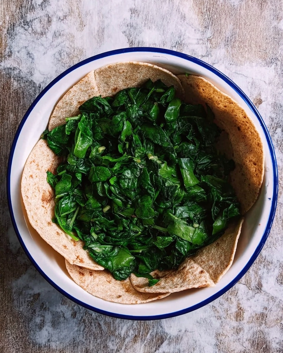 A white round bowl with a blue rim holds a soft whole wheat tortilla that is shaped like a flower with its edges folded inward. Inside this tortilla, there is a layer of rough-textured fresh chopped dark green leafy spinach that covers the bottom evenly. The bowl is placed on a surface with a white marbled texture. photo taken with an iphone --ar 4:5 --v 7