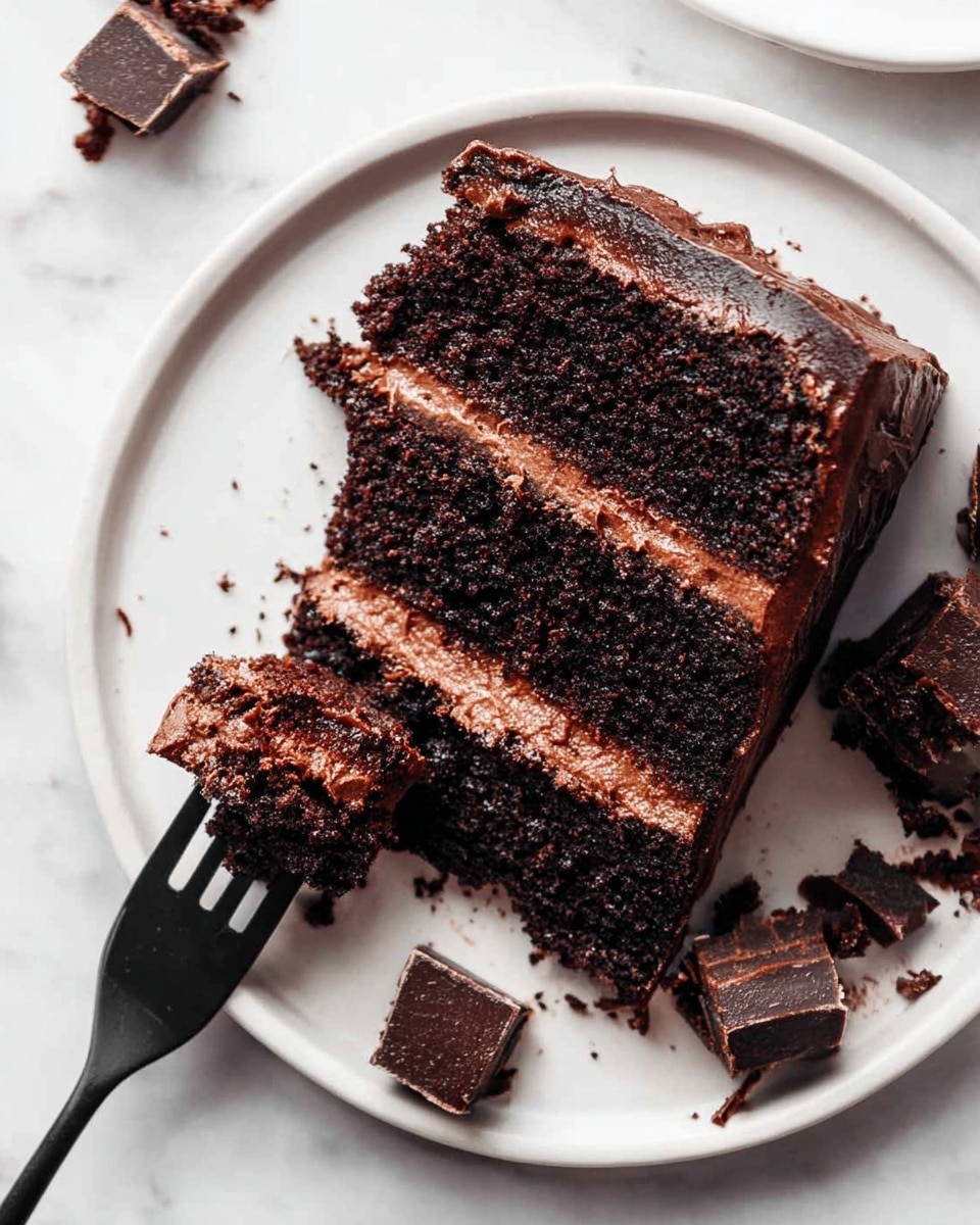 A close-up of a white plate with a two-layer dark chocolate cake slice, each layer separated by a smooth, lighter chocolate cream filling. The cake layers look moist with a rich, slightly crumbly texture. A black fork holds a small bite-sized piece of the cake, resting near the slice on the plate. Around the plate on a white marbled surface, there are several small chocolate cake cubes scattered. The photo is bright, showing the deep brown colors of the cake against the clean white plate and background, photo taken with an iphone --ar 4:5 --v 7