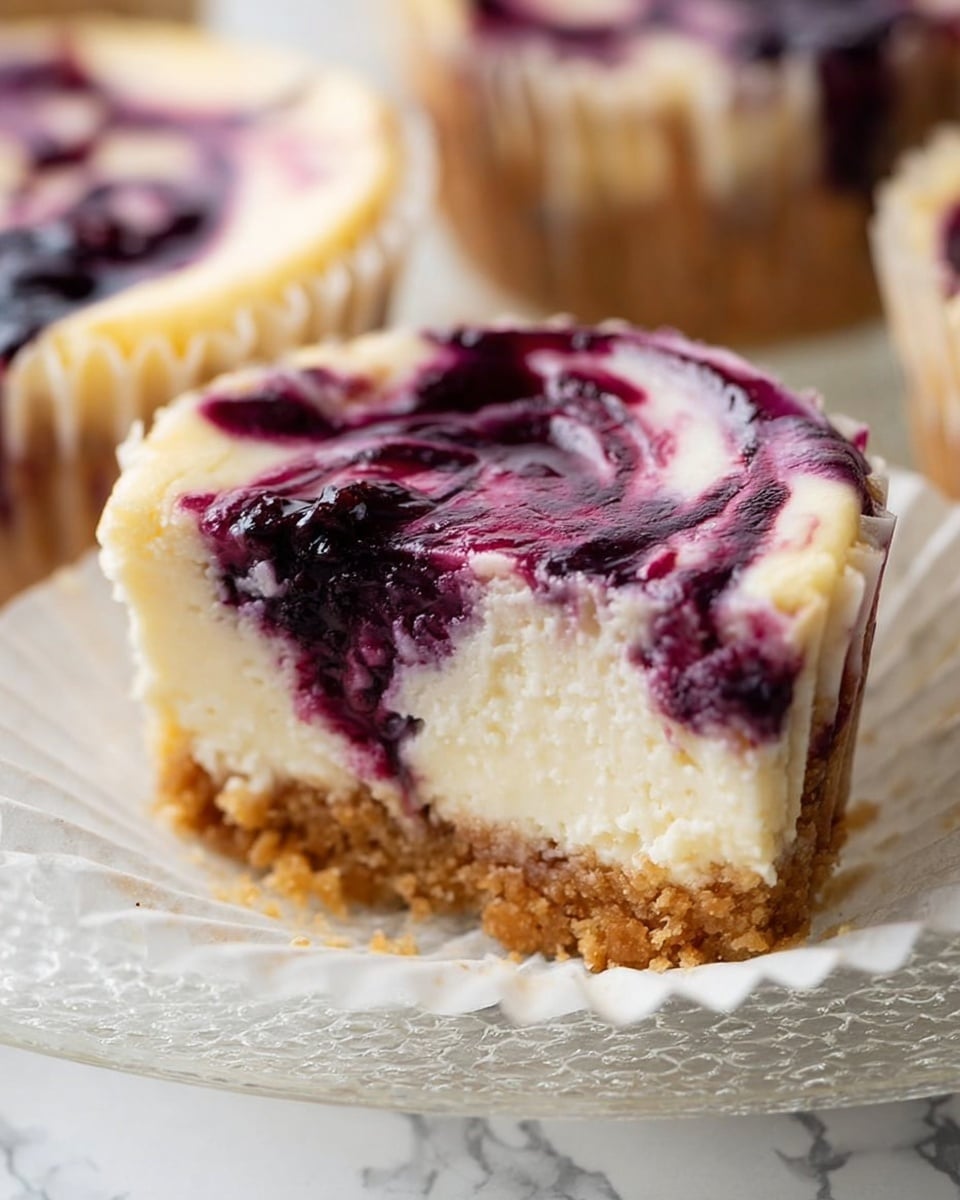 The image shows a close-up of a mini blueberry cheesecake with three distinct layers. The bottom layer is a crumbly light brown crust, followed by a thick creamy off-white cheesecake middle layer with a smooth texture. On top, there is a swirling layer of purple blueberry sauce, mixed lightly into the cheesecake. The cheesecake is in a white paper cup liner placed on a clear textured glass plate. The background has a white marbled texture. Photo taken with an iphone --ar 4:5 --v 7