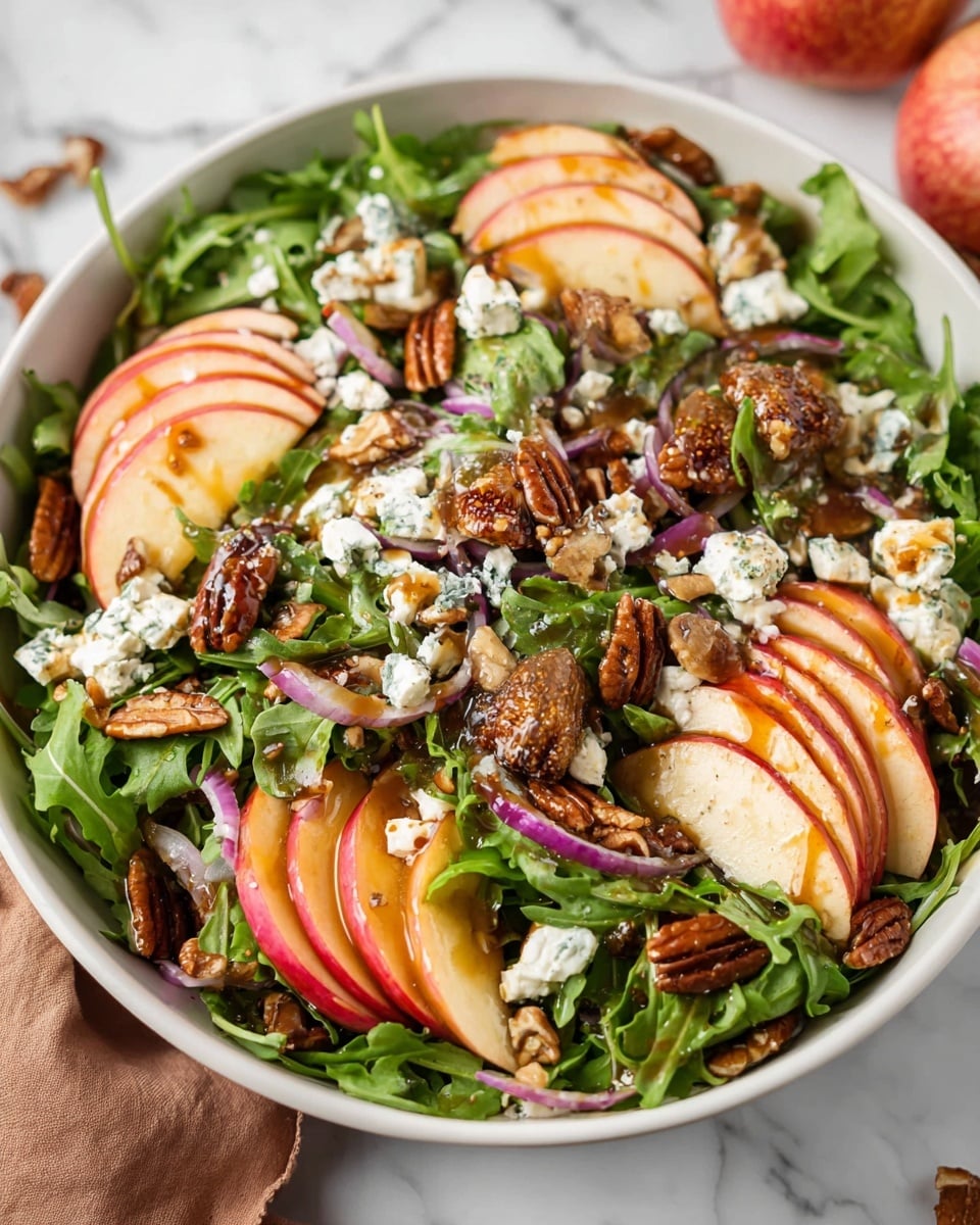 A white bowl filled with a fresh salad on a white marbled surface, layered with green leafy arugula at the bottom, topped with thin slices of red apple layered evenly around the bowl. Scattered on top are brown pecan halves and small chunks of white feta cheese. There are also some thin slices of purple-red onion mixed in, with a few pieces of chopped figs visible. A brown dressing is drizzled over the salad, adding a shiny texture to parts of the fruit and nuts. Photo taken with an iphone --ar 4:5 --v 7