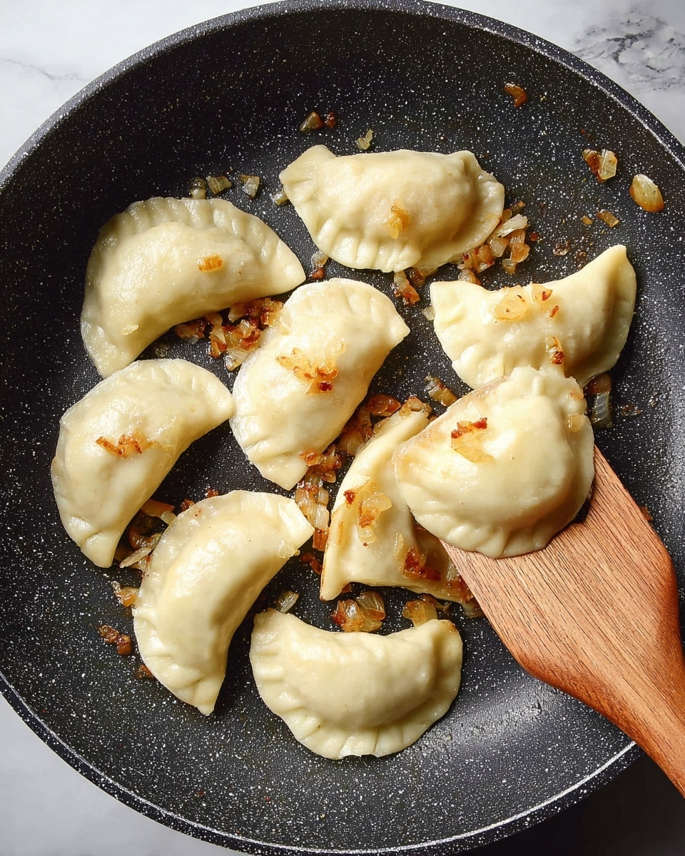 The image shows a black frying pan with a speckled texture, containing nine light golden dumplings arranged in a circular pattern. Each dumpling has a soft, smooth surface with slight ridges on the edges, and small golden brown bits of sautéed onions are scattered around and on top of them. A wooden spatula is placed in the pan, partially sliding under one dumpling on the right side. The pan rests on a white marbled surface. photo taken with an iphone --ar 4:5 --v 7