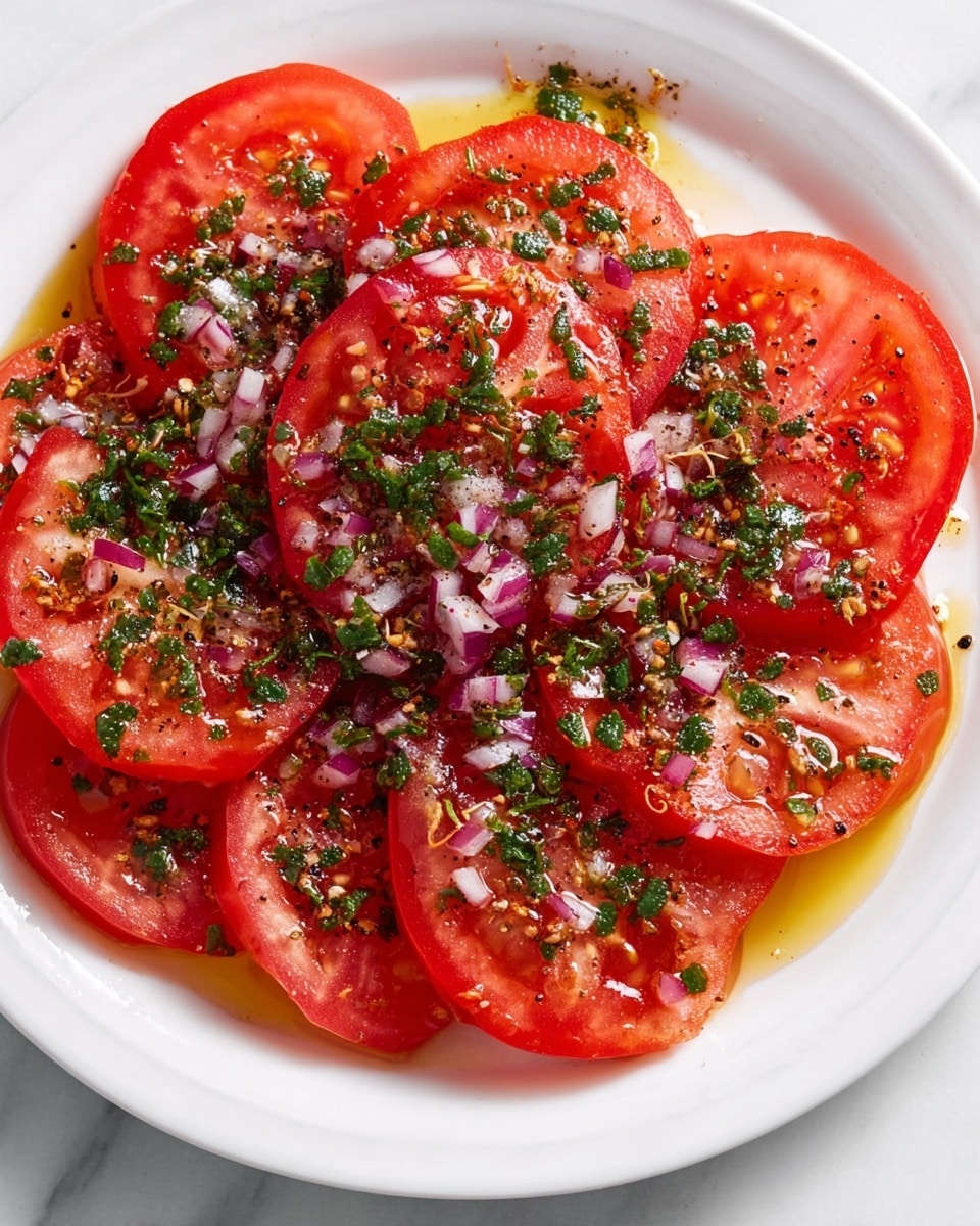 A white plate holds one layer of bright red, thinly sliced tomatoes arranged in a slightly overlapping circle. The surface of the tomatoes is covered with small bits of green herbs and finely chopped purple-red onions, scattered evenly on top. A light drizzle of golden olive oil glistens across the tomatoes, mixing with tiny sprinkles of black pepper and salt, adding texture and shine. The plate sits on a white marbled surface. photo taken with an iphone --ar 4:5 --v 7