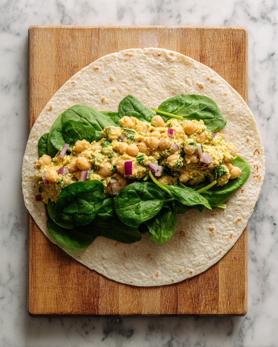 A soft light beige tortilla lies flat on a wooden cutting board with a layer of yellowish, chunky chickpea salad spread evenly across it, mixed with small pieces of red onion and green herbs. On top of the chickpea layer, a bunch of fresh, bright green spinach leaves are spread across the bottom half. In the second image, the bottom half of the tortilla is folded up over the spinach and chickpea salad, showing the textured, slightly uneven fold of the light beige tortilla against the wooden board. The background is a white marbled texture. Photo taken with an iphone --ar 4:5 --v 7