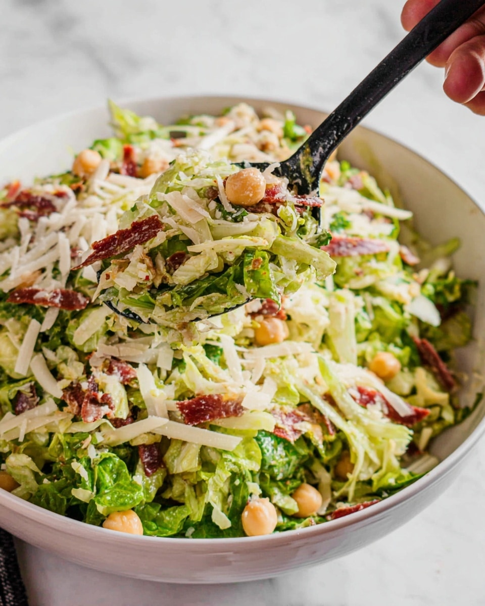 This image shows a mixed salad in a white bowl on a white marbled surface. The salad has multiple layers: a base of thin, chopped green lettuce strips, scattered round beige chickpeas, thin white cheese shreds, light yellow small pieces, and thin slices of reddish-brown meat or dried meat strips mixed throughout. A black spoon lifts some salad from the bowl, with a woman's hand holding the bowl on the right edge of the image. Photo taken with an iphone --ar 4:5 --v 7