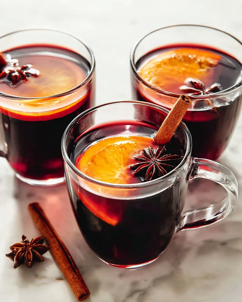 Three clear glass mugs are filled with dark red mulled drink, each containing a thick orange slice floating inside near the top edge. Each mug also holds a cinnamon stick standing upright and a star anise placed on the surface, giving texture with its star shape. The mugs rest on a white marbled surface with soft light reflections on the glass, showing a warm, cozy feel. One cinnamon stick lies on the surface beside the mugs. The photo taken with an iphone --ar 4:5 --v 7