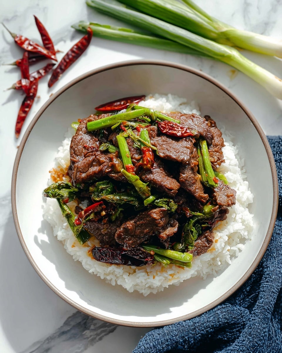 A white plate holds a bed of white steamed rice as the bottom layer, with medium-thin slices of brown cooked beef layered on top, covered in a glossy sauce. Bright green chopped scallions and whole red dried chilies are mixed throughout the beef, adding texture and color contrast. The beef has a slightly wrinkled texture and a rich, shiny coating from the sauce, with the vegetables scattered evenly across the dish. The surface beneath the plate is white marbled texture. photo taken with an iphone --ar 4:5 --v 7
