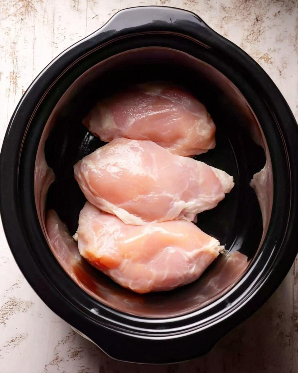 A black slow cooker bowl filled with a cooked dish showing three main layers: the bottom layer is a dark brown sauce mixed with black beans and corn, the middle layer has shredded light brown chicken spread evenly, and the top layer is a mix of shredded yellow cheese and fresh green cilantro leaves scattered around. The background is a white marbled texture with a white tiled wall visible behind. Photo taken with an iphone --ar 4:5 --v 7