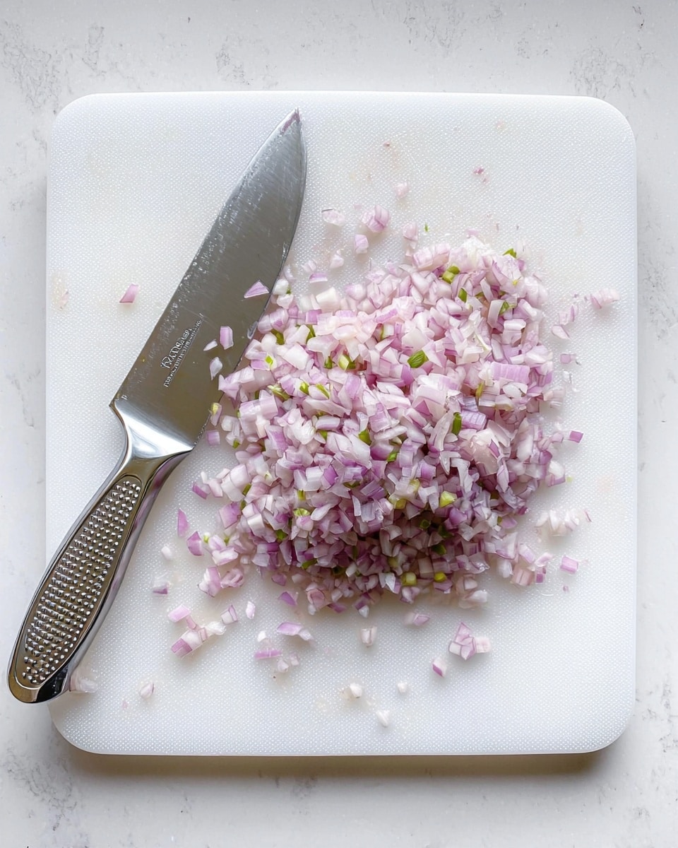The image shows a white cutting board on a white marbled surface. On the cutting board is a pile of finely chopped light purple shallots with small bits of green. To the left of the chopped shallots lies a shiny silver knife with a dotted handle, resting flat on the board. There are small pieces of shallot stuck on the knife blade. The whole scene is clean and simple. photo taken with an iphone --ar 4:5 --v 7