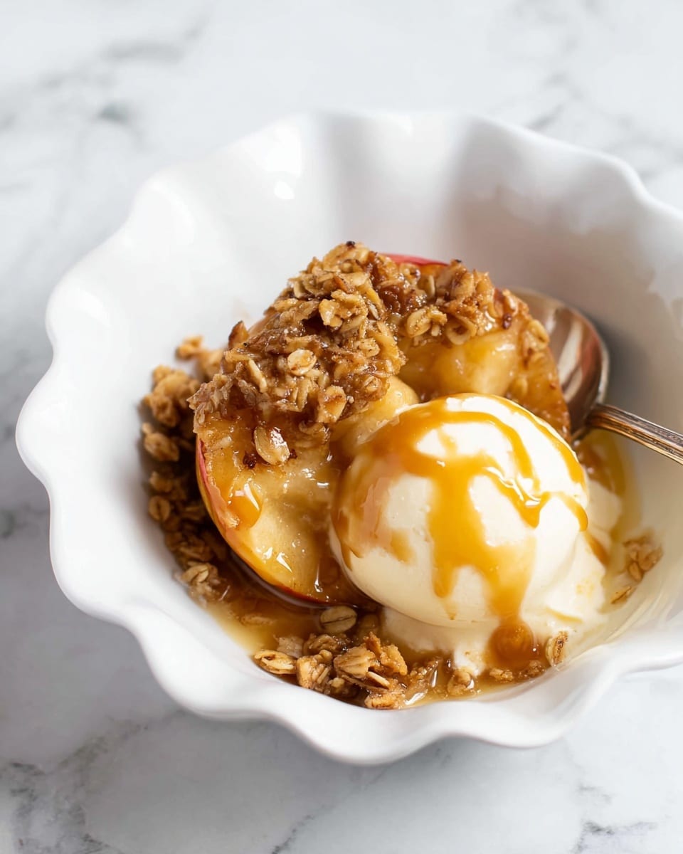 A white scalloped bowl holds a baked apple sliced in half, topped with a golden brown oat crumble that looks crunchy and soft with a shiny caramel drizzle. Next to the apple is a scoop of creamy white ice cream with caramel sauce drizzled on top. A fork is partly visible on the right side, with some oat crumble pieces resting on it. The bowl sits on a white marbled surface. Photo taken with an iphone --ar 4:5 --v 7
