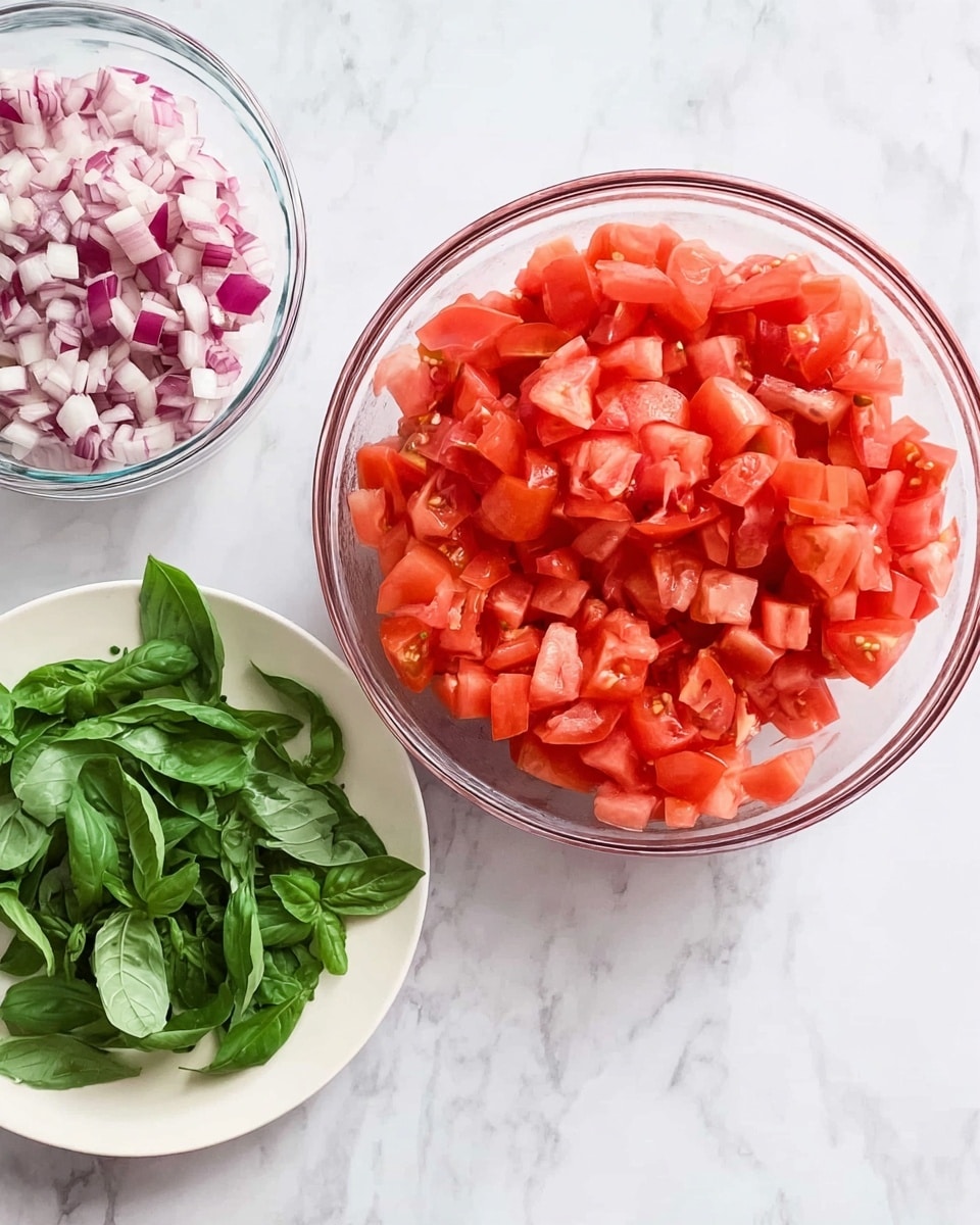 The image shows three bowls on a white marbled surface. The largest bowl is clear glass and filled with bright red chopped tomatoes, taking most of the space in the frame. Below it, there is a white plate with fresh green basil leaves that look soft and slightly shiny. Towards the top left corner, part of a clear glass bowl with finely chopped red onions is visible, showing small purple and white pieces. The colors are natural and bright, highlighting fresh ingredients. photo taken with an iphone --ar 4:5 --v 7