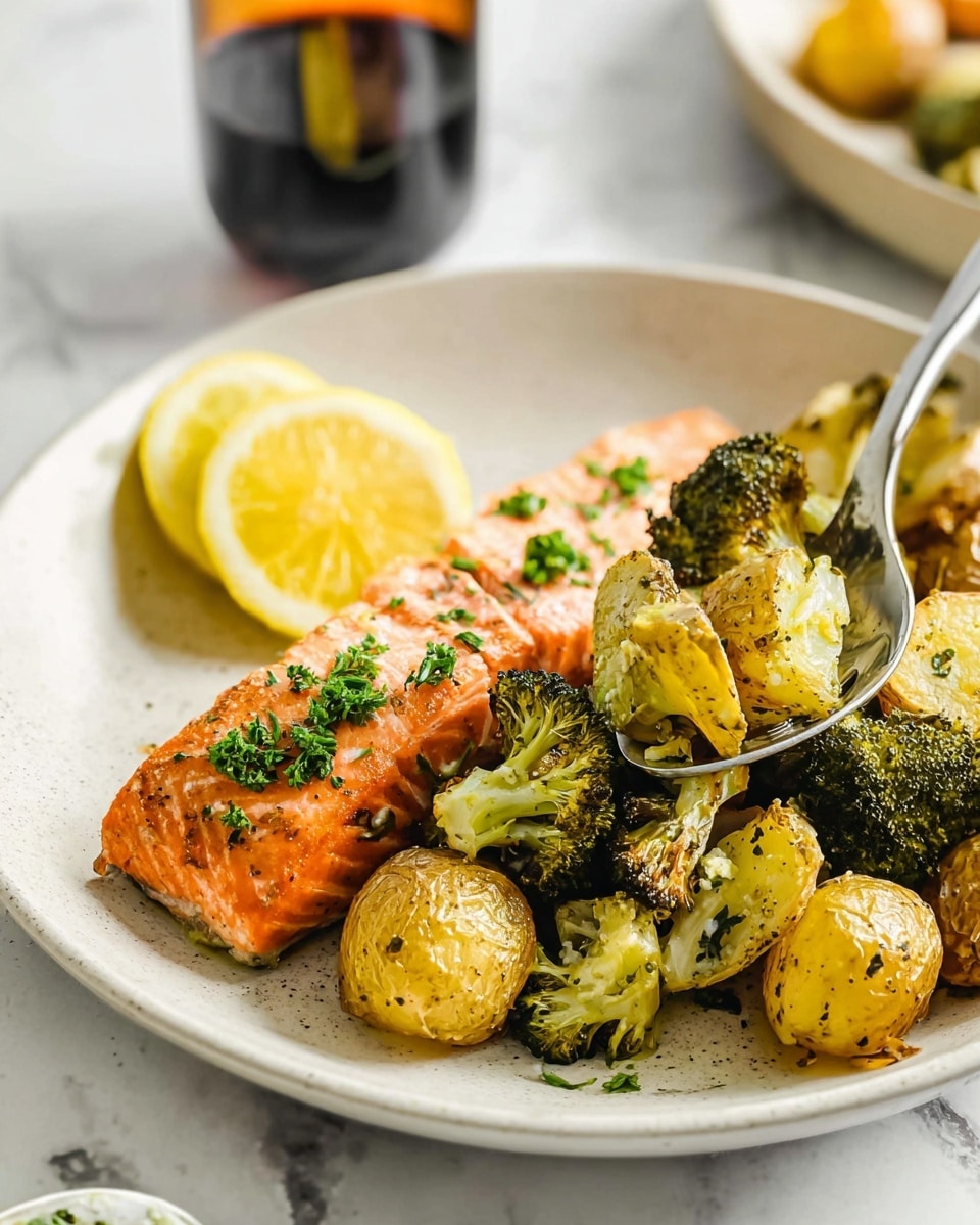 The image shows a white round plate with two main layers: at the bottom, there are roasted golden-brown baby potatoes mixed with green broccoli pieces, seasoned with herbs, giving a speckled texture. On top of these vegetables, there is a perfectly cooked salmon fillet with an orange-pink color, sprinkled with small green herb pieces. A bright yellow lemon wedge rests among the vegetables on the left side of the plate. The background is white marbled, with a blurred dark glass with an orange base also visible. A spoon extends into the plate from the right edge, holding the vegetables. Photo taken with an iphone --ar 4:5 --v 7