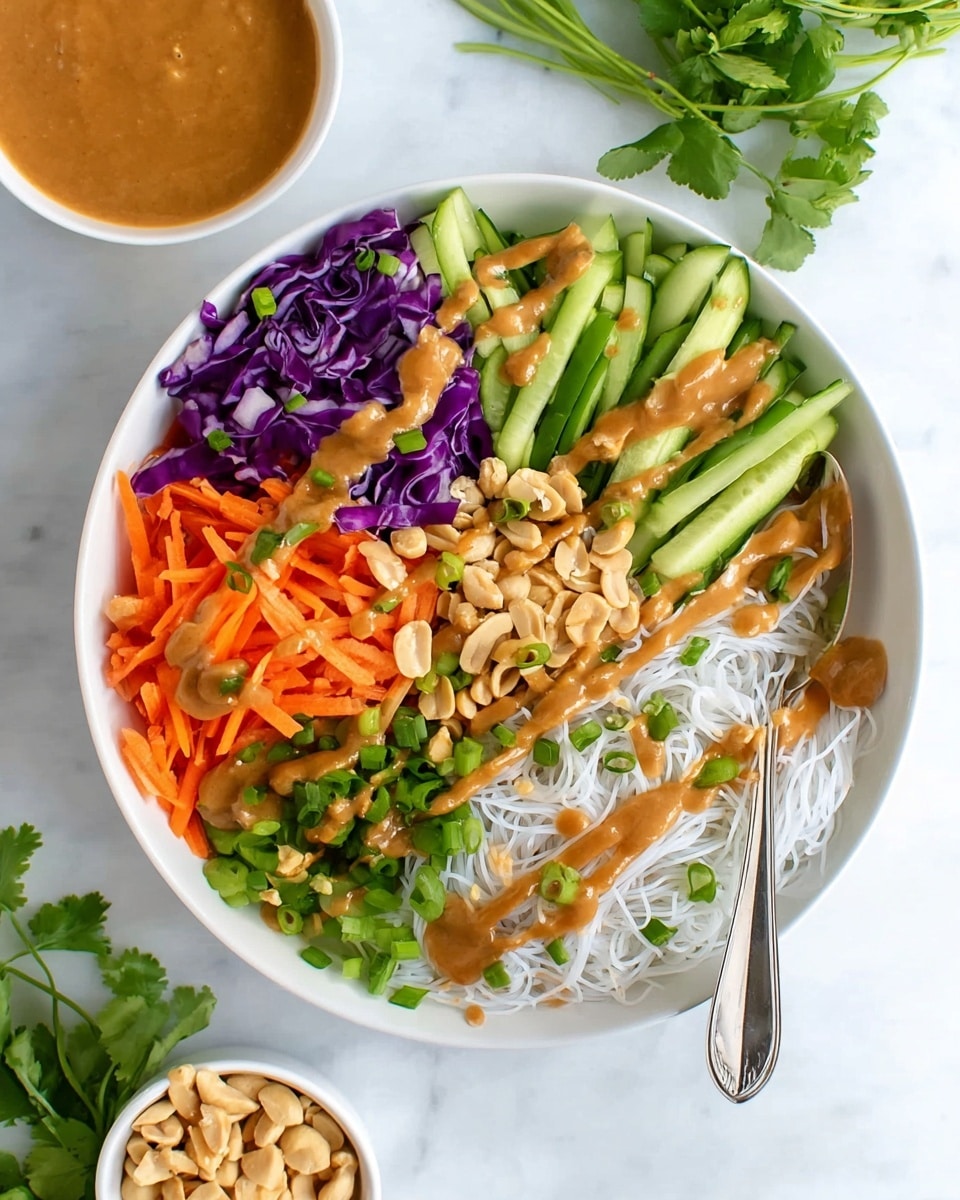 A white bowl filled with a colorful layered dish starting with a base of thin white noodles spread evenly. On top, bright green cucumber sticks are placed on one side, next to vibrant purple cabbage shreds arranged neatly. Adjacent to the cabbage, there are thinly sliced orange carrot sticks, and beside them, chopped green onions form another layer. In the middle, a handful of light brown peanuts is sprinkled over the vegetables. A smooth brown sauce is drizzled generously across all layers, creating lines that stretch over the noodles and vegetables. Small green herb leaves are scattered over the dish. A silver spoon with some sauce rests on the side of the bowl. The bowl sits on a white marbled surface, with fresh green herbs and a small white bowl of extra peanuts and sauce nearby. Photo taken with an iphone --ar 4:5 --v 7