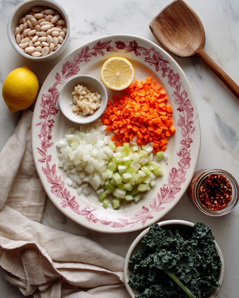 A white oval plate with a pink leaf pattern holds five sections: a small white bowl with minced garlic at the top, finely diced bright orange carrots to the right of it, a pile of finely diced white onions below the garlic, light green diced celery to the left, and a halved lemon placed on top of the celery. Next to the lemon is a small glass jar filled with dark red chili flakes. Below the plate, a beige cloth with soft folds spreads across the white marbled surface. To the bottom right, a white bowl holds dark green leafy kale. On the left side of the image, there is a small white bowl filled with white beans and a wooden spoon lying on the cloth. Photo taken with an iphone --ar 4:5 --v 7