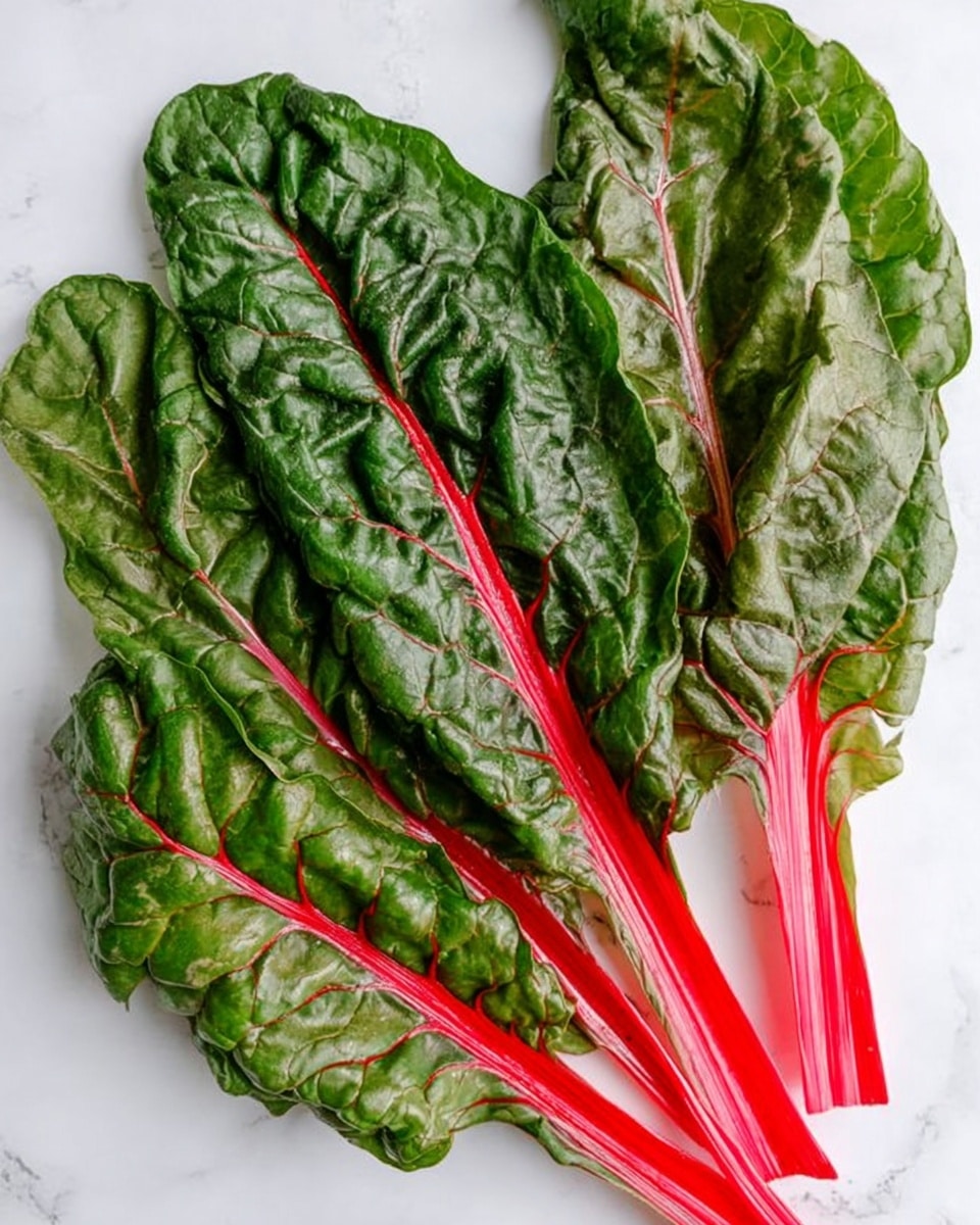 The image shows five large leaves of Swiss chard with bright red stems and deep green, wrinkled leaves with visible veins. The leaves are layered on a white marbled surface, spread out slightly overlapping each other with the red stems mostly pointing in the same direction. The texture of the leaves looks fresh and slightly shiny, with each leaf showing thick and prominent red veins running through the green parts. The arrangement is natural and simple, focusing on the vibrant color contrast between the red stems and green leaves. photo taken with an iphone --ar 4:5 --v 7
