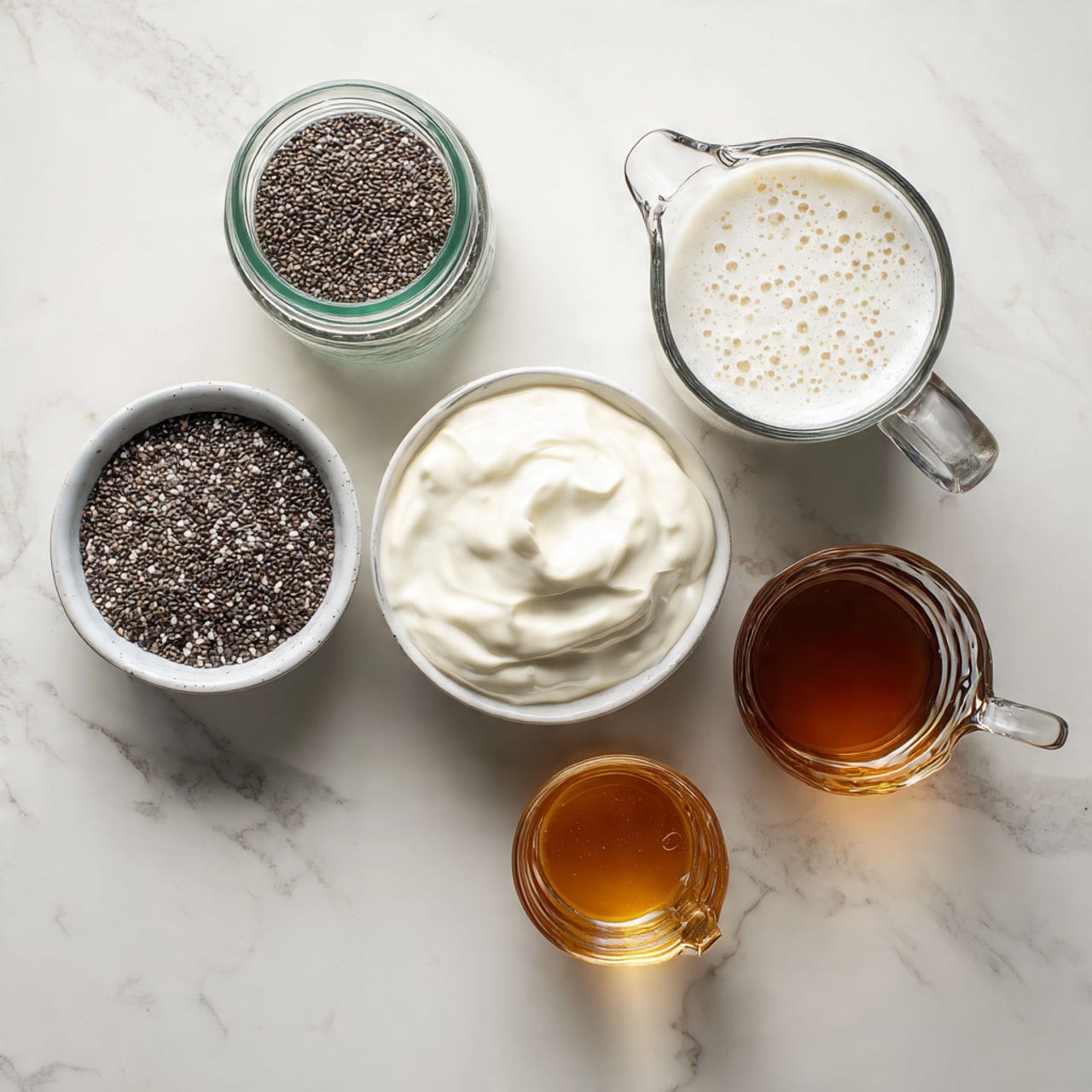 Five containers with ingredients sit on a white marbled surface. At the top left, there is a small glass jar with a green lid. To the right, a measuring glass with a handle holds white creamy liquid with small bubbles on top. Below the jar is a white bowl filled with thick, smooth, white yogurt. In the center near the bottom, a white bowl contains small black and white chia seeds, showing a rough texture. To the right of the seeds, a small clear glass cup with a handle is filled with dark amber liquid. The containers are evenly spaced and the photo has soft natural light. photo taken with an iphone --ar 4:5 --v 7