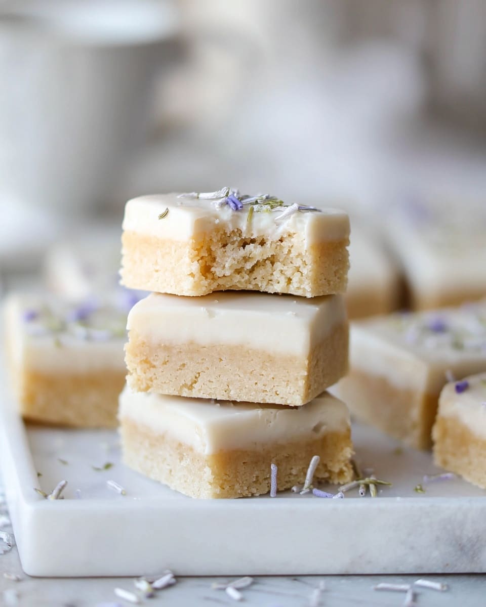 The image shows a stack of three square bars on a white tray with a white marbled surface underneath. Each bar has two layers: a thick, crumbly beige base and a smooth white icing layer on top. The top bar has a bite taken out, revealing the soft texture inside. Small purple and green sprinkles are scattered on the icing. More similarly iced bars are visible in the background, softly blurred. The lighting is bright and natural, highlighting the creamy and textured details of the bars. photo taken with an iphone --ar 4:5 --v 7