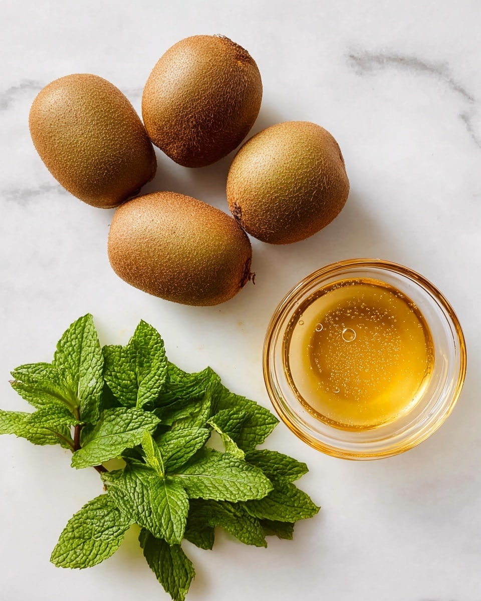 The image shows five whole kiwis with a rough brown skin placed on a white marbled surface on the left side. On the right side, there is a small clear glass bowl filled with golden honey with air bubbles visible inside. Below the bowl, a fresh small bunch of green mint leaves with textured veins lies flat on the surface. The composition is simple with the kiwis grouped closely together, the bowl near the center-right, and the mint leaves slightly overlapping each other at the bottom right. The background is a smooth white marble that softly reflects the light. photo taken with an iphone --ar 4:5 --v 7