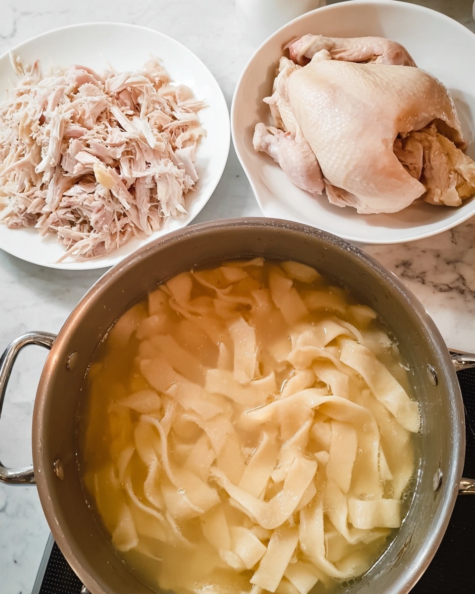 The image shows a pot filled with light beige homemade thick noodles cooking in a clear broth, with noodles floating and layered unevenly in the liquid. Behind the pot, there are two white plates; one plate has shredded pale pink chicken pieces, and the other plate holds a large portion of cooked chicken with tender, soft skin and some meat pulled apart. The setting is on a white marbled surface with part of the stovetop visible. Photo taken with an iphone --ar 4:5 --v 7