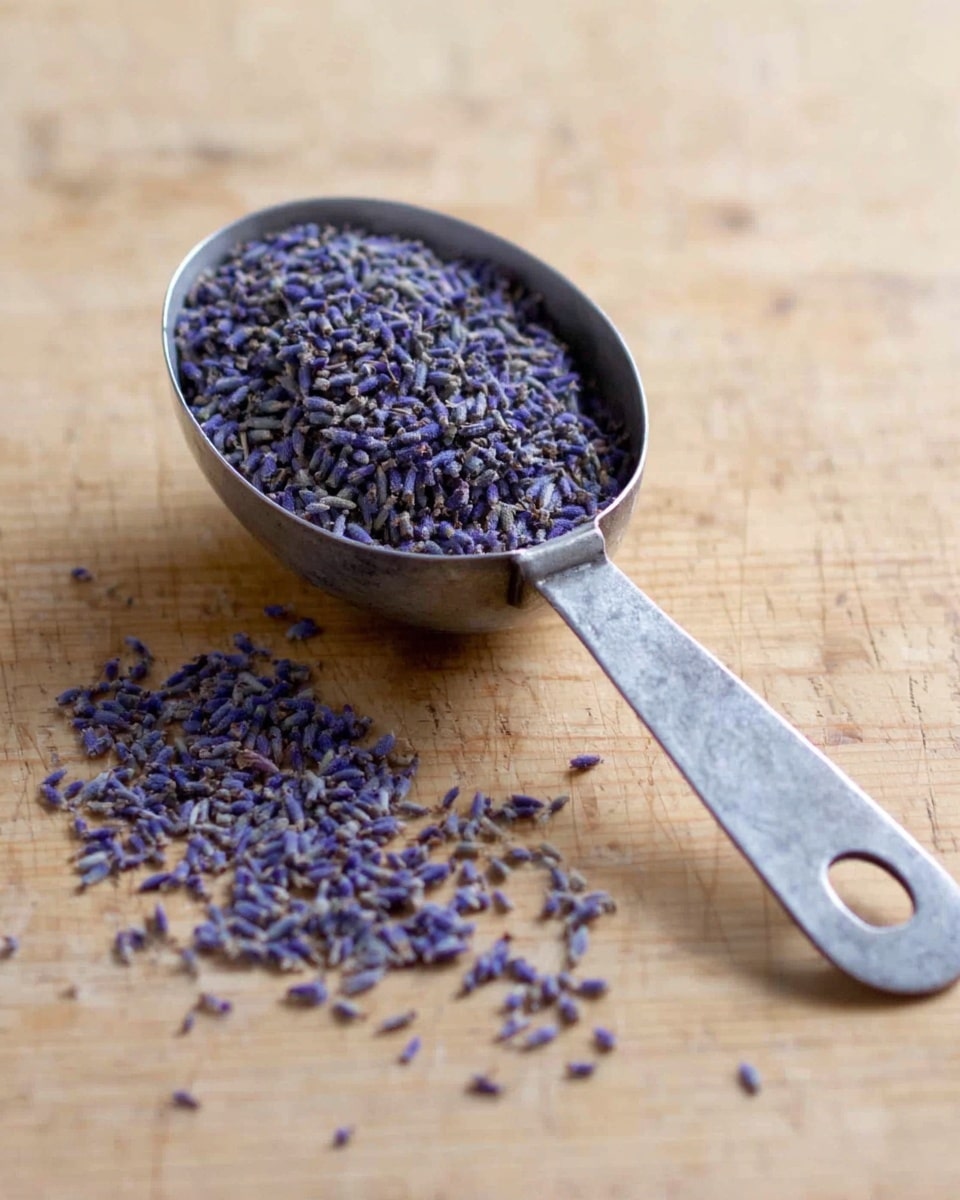 A metal measuring scoop filled with small dried purple lavender buds is placed on a wooden surface. Some lavender buds have spilled out in front of the scoop, showing their delicate small shapes and muted purple color. The handle of the scoop extends to the right with a small hole near its end. The wood underneath has a natural light brown tone and soft grain texture. photo taken with an iphone --ar 4:5 --v 7