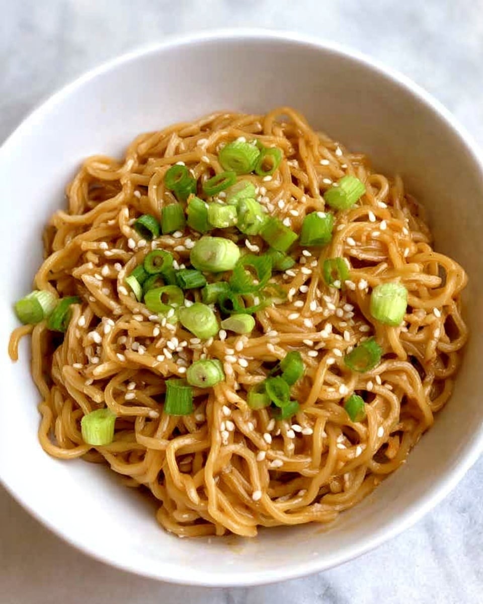 A white bowl holds a serving of cooked noodles that are light brown and slightly shiny, showing they are coated in sauce. The noodles are topped with small white sesame seeds sprinkled evenly and chopped green onions with green and white parts, adding fresh color and texture. The bowl is placed on a white marbled surface that shows soft veins and light reflections. photo taken with an iphone --ar 4:5 --v 7