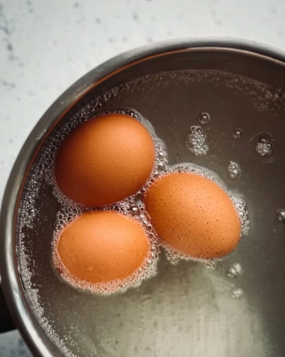 Three brown eggs are shown inside a silver pot filled with boiling water. The eggs have tiny bubbles clinging to their smooth shells, and the water surface is filled with small, clear bubbles rising up. The silver pot has a brushed metal texture and the background is a white marbled surface. photo taken with an iphone --ar 4:5 --v 7