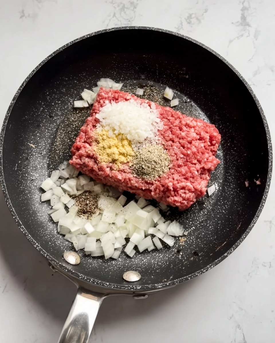 A black frying pan with a metal handle is on a white marbled surface. Inside the pan, there is a block of raw ground meat placed in the center. On top of the meat, there are three piles of seasoning: finely chopped white onion on the right, a light yellow powder seasoning near the top left, and a small black pepper seasoning near the bottom. Additional small pieces of chopped white onion are scattered around the meat inside the pan. Photo taken with an iphone --ar 4:5 --v 7