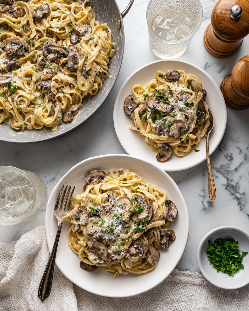 Two white plates hold a serving of thick, looped pasta mixed with sliced brown mushrooms, all coated in a creamy light tan sauce. The pasta is layered thick and winding, topped with small green herbs and a light sprinkle of grated white cheese. A gray pan on the left side holds the rest of the pasta with the sauce and mushrooms, showing the same thick pasta texture. Around the plates are two clear glasses with ice and water, a wooden pepper grinder, and a small white dish with chopped green herbs. The setting is on a white marbled surface with a white cloth underneath. Photo taken with an iphone --ar 4:5 --v 7