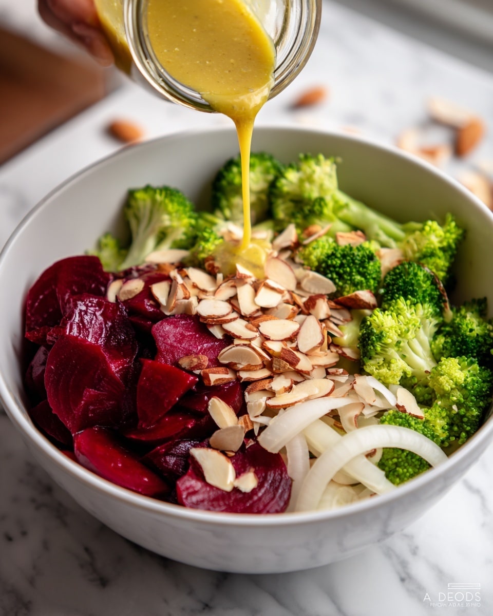 A white bowl is filled with a salad that has three main layers: on the bottom are bright green broccoli pieces, on top of that are thin white onion slices spread out, and the top layer features dark red beet slices arranged on one side. Scattered over the salad are thin, light brown slivered almonds. A small jar is tilted over the bowl, pouring a golden yellow dressing onto the beet slices. The scene is set on a white marbled surface, with part of a woman's hand holding the jar. Photo taken with an iphone --ar 4:5 --v 7