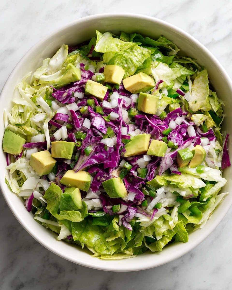 A bowl full of fresh salad made with green lettuce leaves forming the base layer, mixed with chopped white cabbage and purple cabbage pieces scattered throughout. Small cubes of pale green avocado sit on top, along with bits of diced white onion and green bell pepper spread evenly across the salad. The bowl holding the salad is white, placed on a white marbled surface. photo taken with an iphone --ar 4:5 --v 7