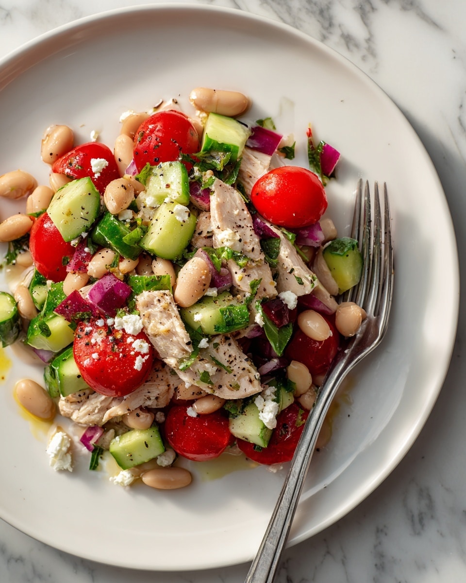 A white plate holds a colorful salad with different layers and textures. The base layer has chunks of light beige beans mixed with pieces of pale cooked chicken. On top, there are bright red halved cherry tomatoes and fresh green cucumber chunks cut into small pieces. Scattered throughout are bits of purple-red onion and small white crumbles of cheese. The salad is lightly sprinkled with black pepper and fresh green herbs, adding specks of color and seasoning. The plate is set on a white marbled surface, and a silver fork rests on the right edge of the plate. photo taken with an iphone --ar 4:5 --v 7