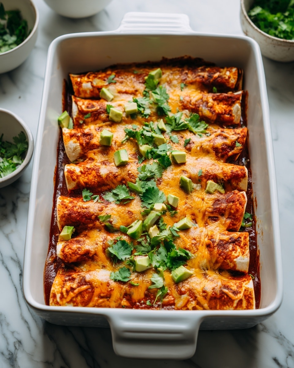 A white rectangular baking dish is filled with six rolled enchiladas layered side by side, covered in a melted light orange cheese that has browned slightly in spots, giving a textured appearance on top. The enchiladas have a reddish sauce visible around the edges underneath the cheese. Scattered on top are small chunks of bright green avocado and fresh green cilantro leaves, adding a fresh contrast to the warm tones of the dish. The background shows a white marbled surface with blurred white bowls containing green leafy elements, enhancing the homemade feel of the meal. photo taken with an iphone --ar 4:5 --v 7