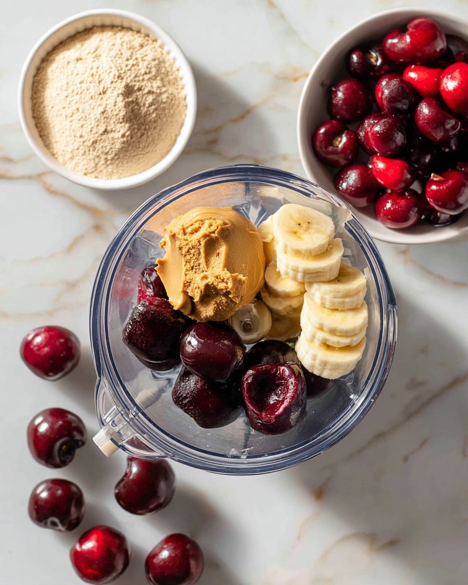 Inside a clear blender cup, there are four main layers of ingredients: at the bottom are dark red cherries, on top of that is a layer of light yellow banana slices, then a scoop of light brown peanut butter sits beside a heap of pale beige powder. Around the blender cup, some loose dark red cherries are scattered on a white marbled surface. To the top left, there is a small white bowl holding more light beige powder, and to the top right, a white bowl filled with a mix of shiny dark red and bright red cherries. The scene is bright and clean, photo taken with an iphone --ar 4:5 --v 7