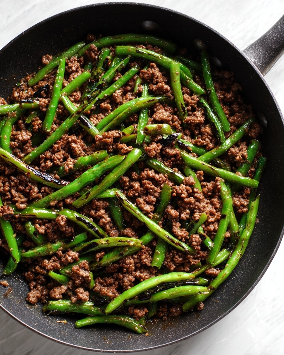 A black pan filled with cooked ground beef topped with green beans that are lightly charred, scattered evenly throughout the beef. The beef has a coarse texture with small chunks and a dark brown color, while the green beans are a vibrant green with some dark grill marks, adding contrast. The pan sits on a white marbled surface. photo taken with an iphone --ar 4:5 --v 7