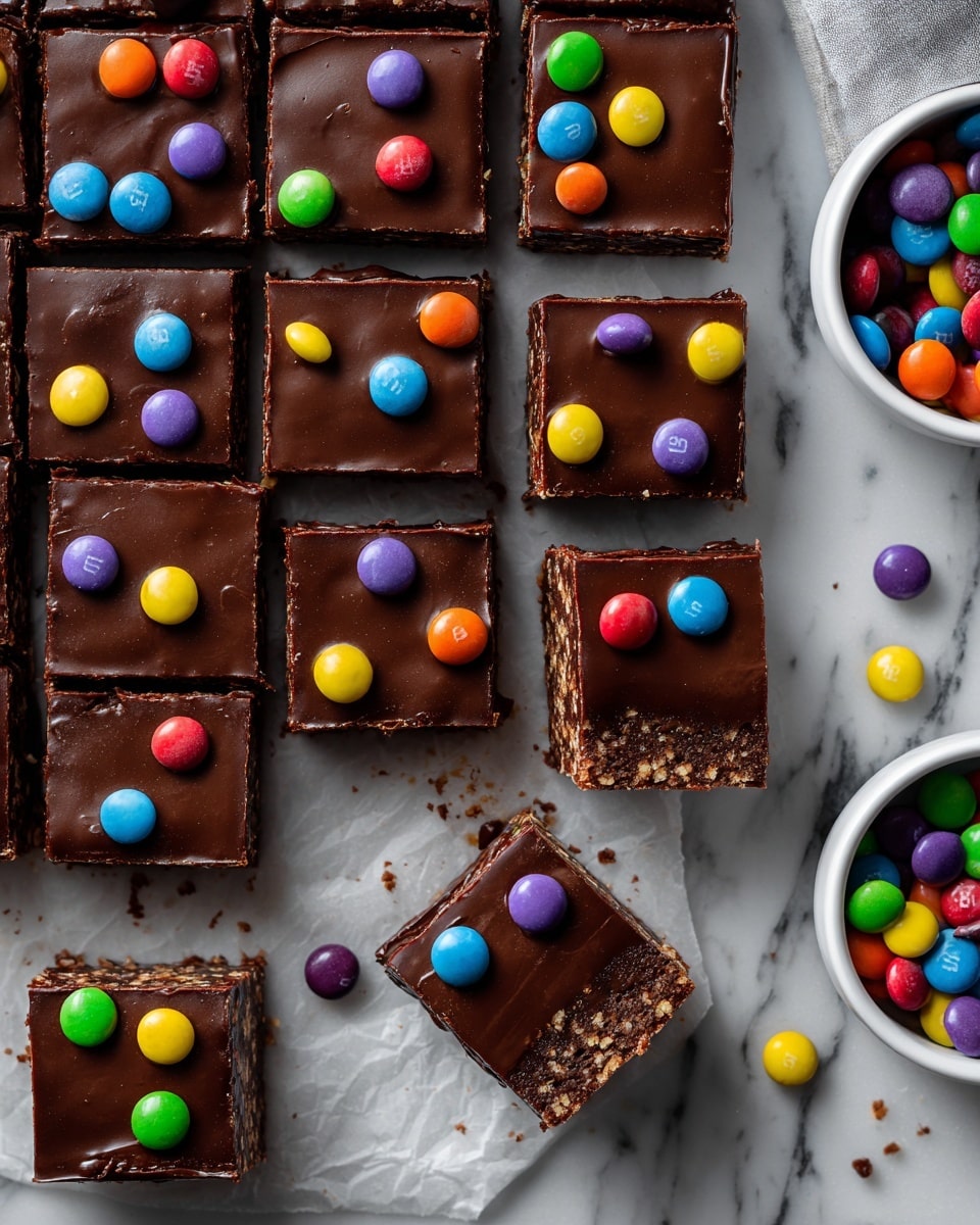 The image shows square pieces of chocolate dessert arranged in a grid on a white marbled surface. Each piece has two visible layers: a dark, dense bottom layer with a crumbly texture and a smoother, thick top layer of shiny chocolate ganache. The top is decorated with small colorful candy pieces in red, yellow, green, blue, purple, and orange scattered evenly. One square is lifted to show the side view clearly, and there are white bowls with more colorful candies partially visible on the right and bottom sides. A few candies are scattered around the squares on the surface. photo taken with an iphone --ar 4:5 --v 7