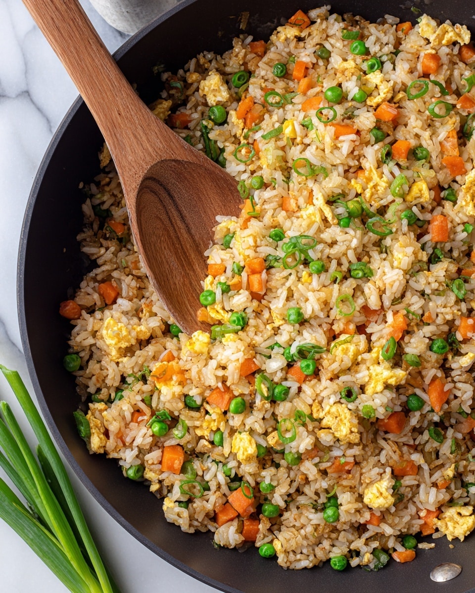 A close-up view of a black pan filled with fried rice made of small rice grains mixed with bright orange carrot cubes, green peas, and sliced green onions, showing a mix of light brown and white pieces of rice and egg. A wooden spoon is partly submerged in the rice, resting on the left side of the pan, sitting on a white marbled surface with a few green onions scattered around. photo taken with an iphone --ar 4:5 --v 7