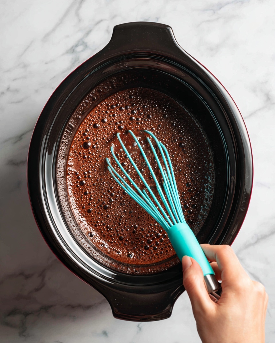 A close-up image of a red slow cooker showing a thick, bubbly chocolate mixture inside. A woman's hand holds a bright turquoise whisk that is partially submerged in the chocolate, mixing the frothy dark brown liquid. The slow cooker has a black rim and handles, and it is placed on a white marbled surface. The bubbles in the chocolate liquid give a textured look, and the lighting highlights the shine on the whisk and the moisture of the mixture, photo taken with an iphone --ar 4:5 --v 7