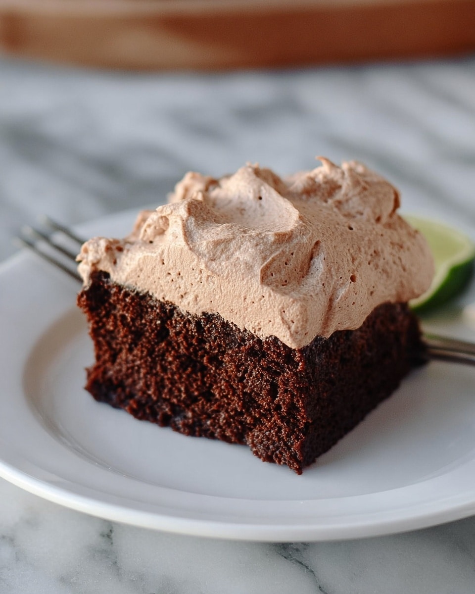 The image shows one piece of chocolate cake on a white plate. The cake has one dark brown layer that looks soft and moist with small air holes. On top of the cake, there is a thick layer of light brown creamy frosting with a textured, fluffy look. The cake sits on a white marbled surface. Photo taken with an iphone --ar 4:5 --v 7