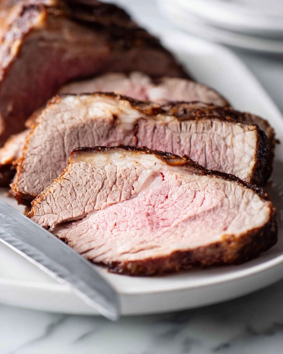 The image shows several thick slices of cooked meat on a white plate placed on a white marbled surface. The meat has three visible layers: a dark brown crust on the outside, a medium brown layer just inside the crust, and a large pink center that looks juicy. The texture of the meat appears soft and tender with some light cracks on the pink part. A serrated knife with a metal blade is positioned to the left side of the plate with the tip close to the meat. The background is softly blurred, keeping the focus on the meat slices. photo taken with an iphone --ar 4:5 --v 7