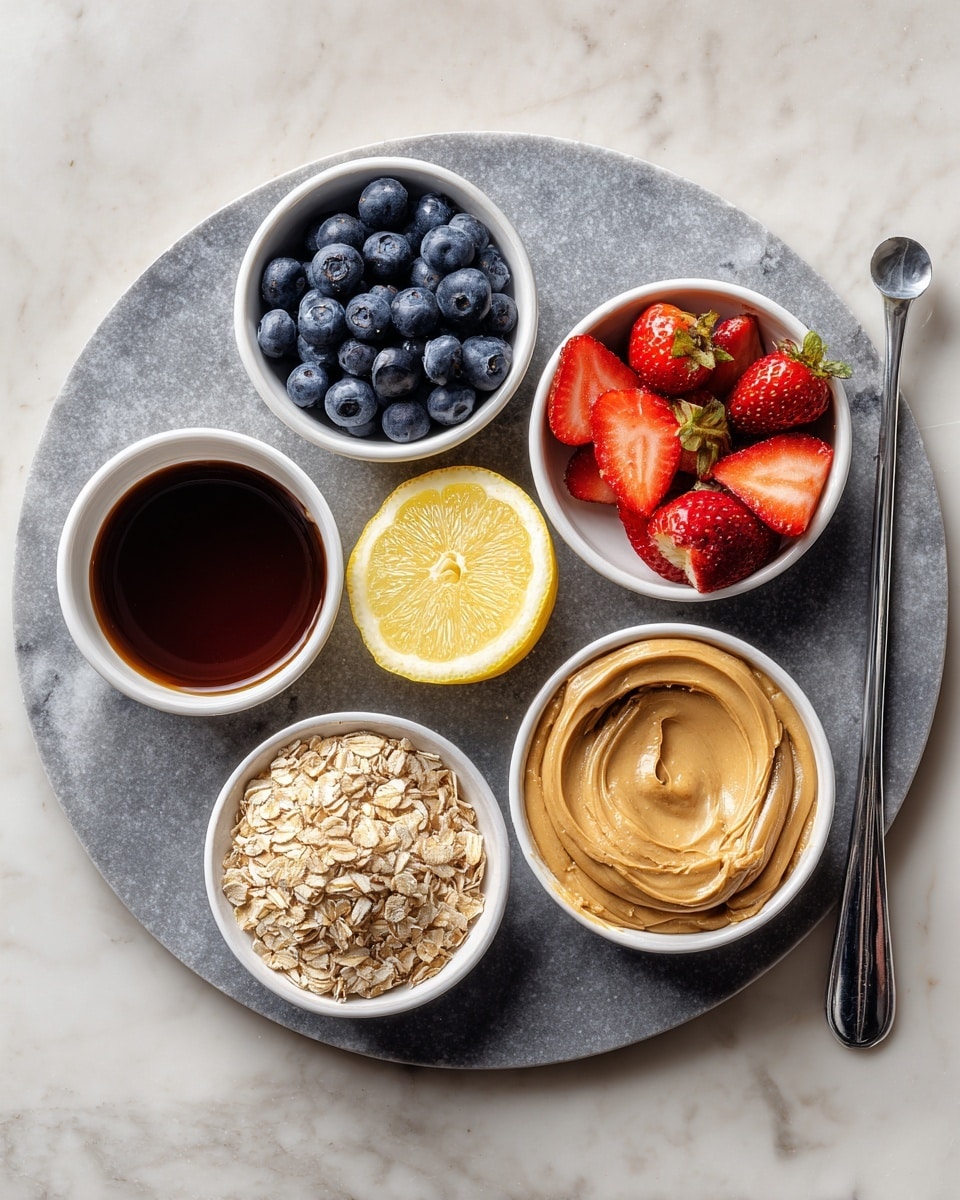 A round gray marble tray holds five small white bowls and a half lemon. The top right bowl is filled with fresh blueberries and sliced strawberries, showing blue and red colors with a shiny texture. Below, there is a bowl filled with dry light brown rolled oats with a rough texture. Next to it on the right, a bowl contains smooth, creamy almond butter in a light brown shade with some swirled patterns. Below that, a bowl of finely ground pale yellow almond flour is seen with a soft, powdery texture. To the left, a small white bowl contains dark amber maple syrup, glossy and smooth. Near the bottom left, a halved lemon shows a bright yellow interior, and a silver measuring spoon filled with vanilla extract sits beside it. The whole setup is on a white marbled surface. Photo taken with an iphone --ar 4:5 --v 7