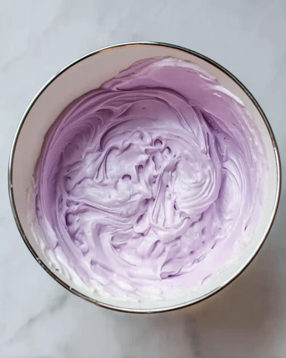 A white bowl filled with a thick, creamy mixture that is light purple in color, with some swirls and folds creating a textured look inside the bowl. The mixture has a glossy finish and soft peaks, showing its smooth and airy texture, placed on a white marbled surface. Photo taken with an iphone --ar 4:5 --v 7