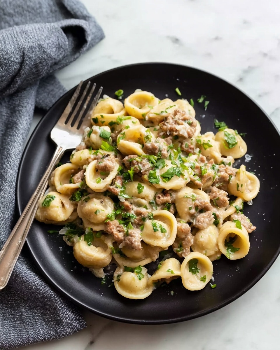 The dish shows a black plate filled with three layers: the bottom layer is pasta shaped like small round discs with hollow centers, light yellow in color and smooth in texture; the middle layer is a creamy sauce mixed with small chunks of browned meat and bits of green herbs spread evenly; the top layer has fresh chopped green herbs sprinkled all over, adding a touch of color contrast. A silver fork rests on the edge of the plate, and a gray cloth napkin is rolled in the background, on a white marbled surface. Photo taken with an iphone --ar 4:5 --v 7