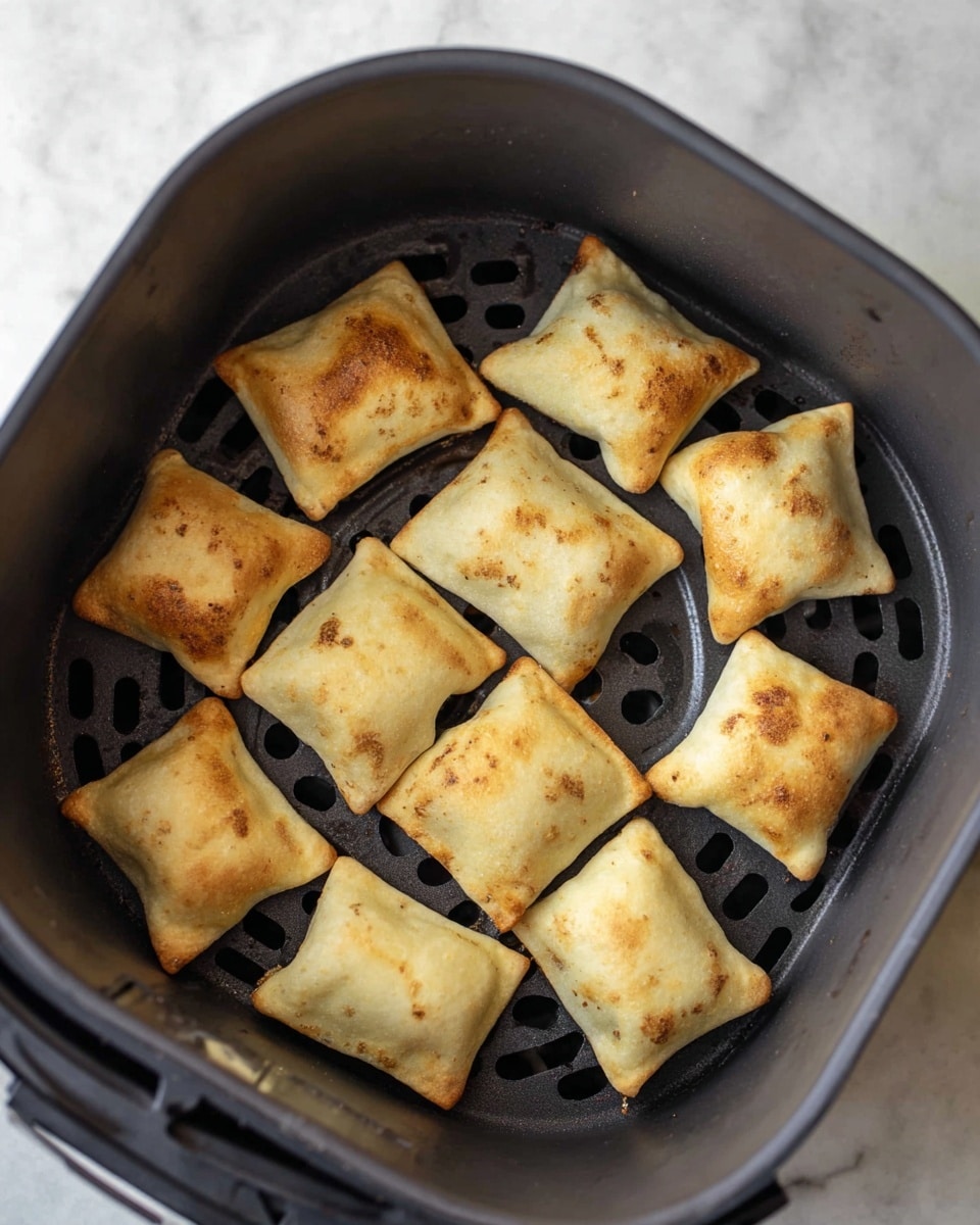 Inside a dark gray air fryer basket on a white marbled surface, there are thirteen light golden brown rectangular pockets arranged loosely in a circular shape. Each pocket has a slightly crispy texture and small browned spots, showing a soft, flaky outer layer. The basket has a patterned base with vent-like cutouts visible between the pillows. The lighting highlights the slight puffiness and even golden tones of the pockets. photo taken with an iphone --ar 4:5 --v 7