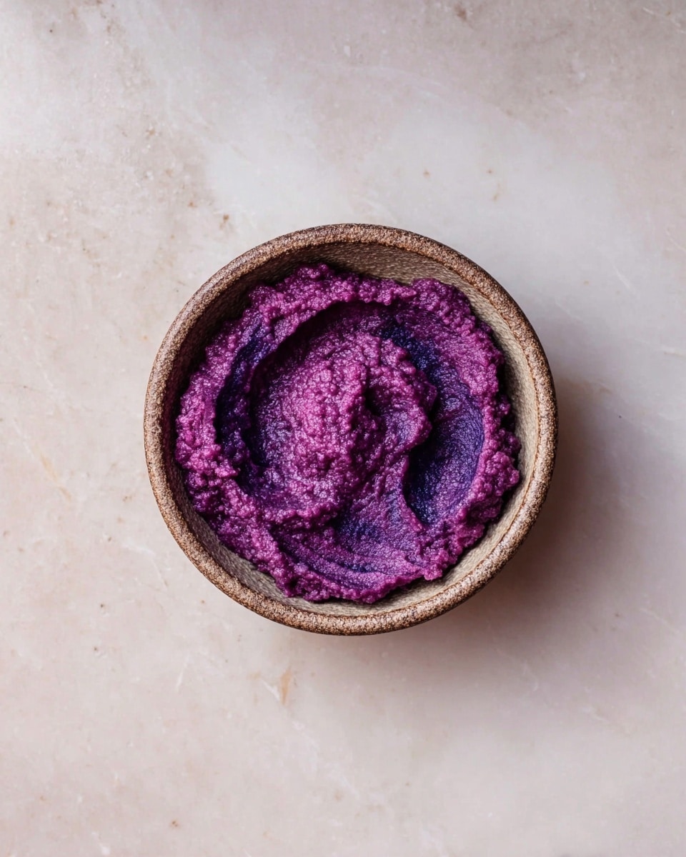A small round bowl with a rough brown edge holds a single layer of thick, bright purple puree. The puree is swirled in the center, showing darker and lighter shades of purple with a textured, slightly grainy surface. The bowl sits on a white marbled surface that adds a clean and smooth contrast. photo taken with an iphone --ar 4:5 --v 7