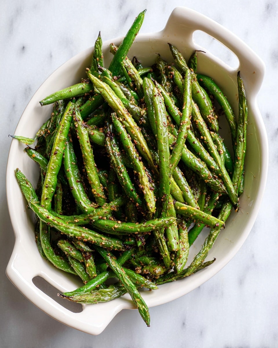 The image shows a white round ceramic dish with two handles, filled with cooked green beans. The green beans are a mix of bright and dark green colors, with some parts slightly browned, showing a roasted texture. They are sprinkled evenly with brownish seasoning, adding a speckled, rough look across the beans. The dish is placed on a white marbled surface, giving a clean and simple background. Photo taken with an iphone --ar 4:5 --v 7