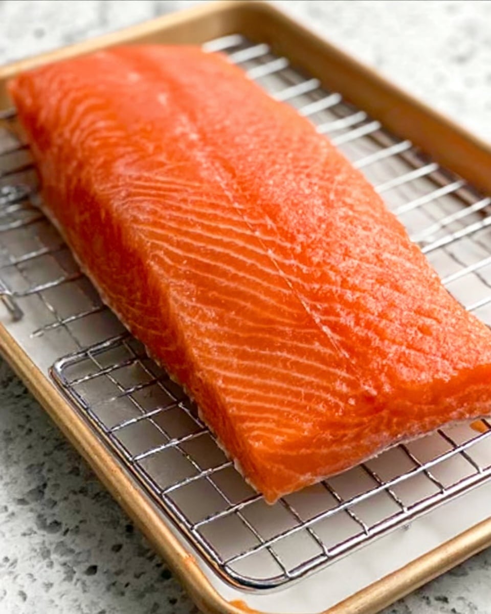 A large, fresh piece of orange salmon with a smooth, slightly shiny surface and fine lines running lengthwise is placed on a metal cooling rack. The rack is set over a white rectangular plate on a white marbled surface. The salmon's texture looks firm and moist, with no other items in the image. Photo taken with an iphone --ar 4:5 --v 7