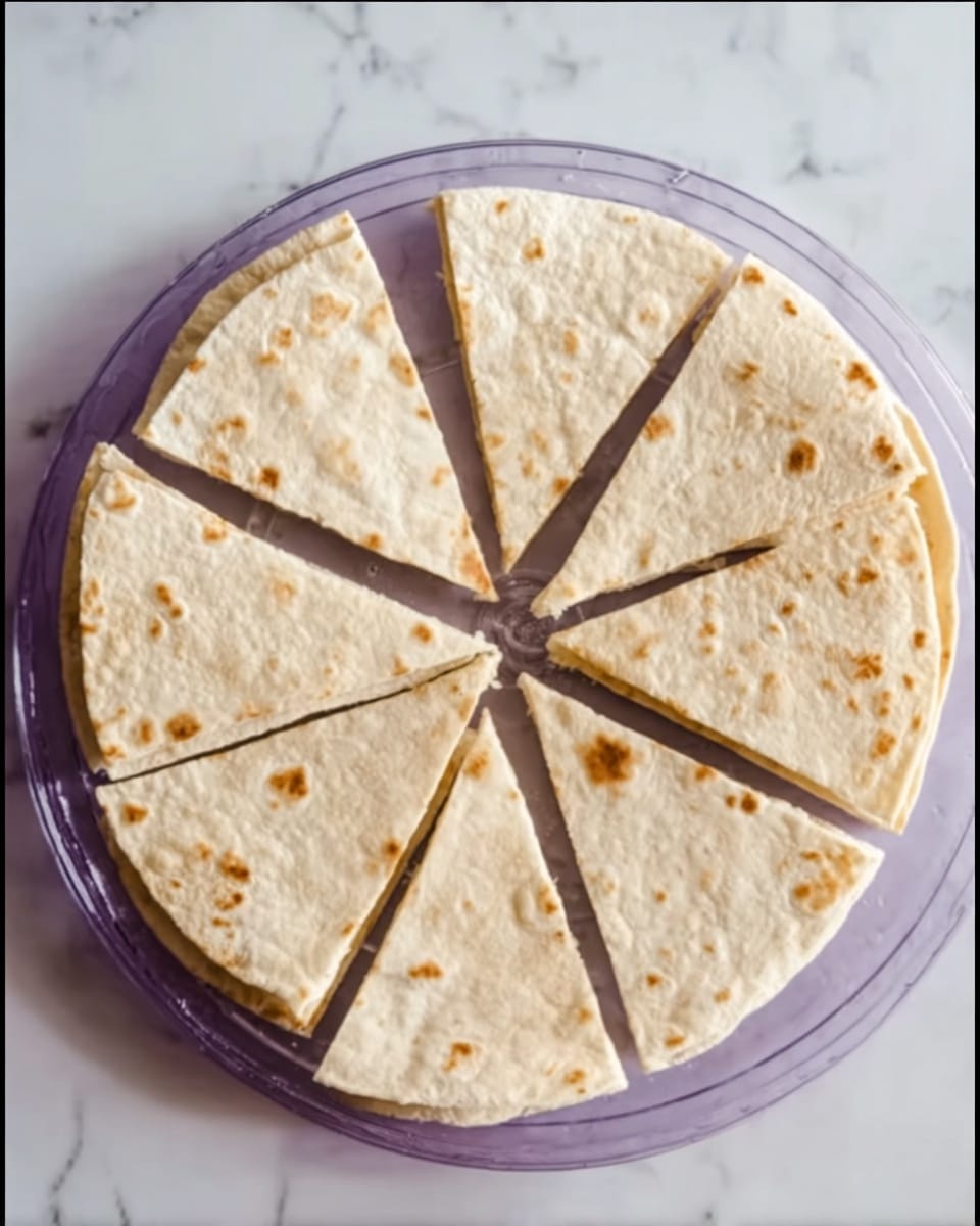 A round tortilla is placed on a clear, purple round plate, sliced into eight equal triangular pieces. The tortilla is pale beige with small brown spots scattered across its surface, showing a slightly dry texture. The pieces are arranged closely in a circle, with the center meeting at a small gap in the middle. The scene is set on a white marbled surface. Photo taken with an iphone --ar 4:5 --v 7