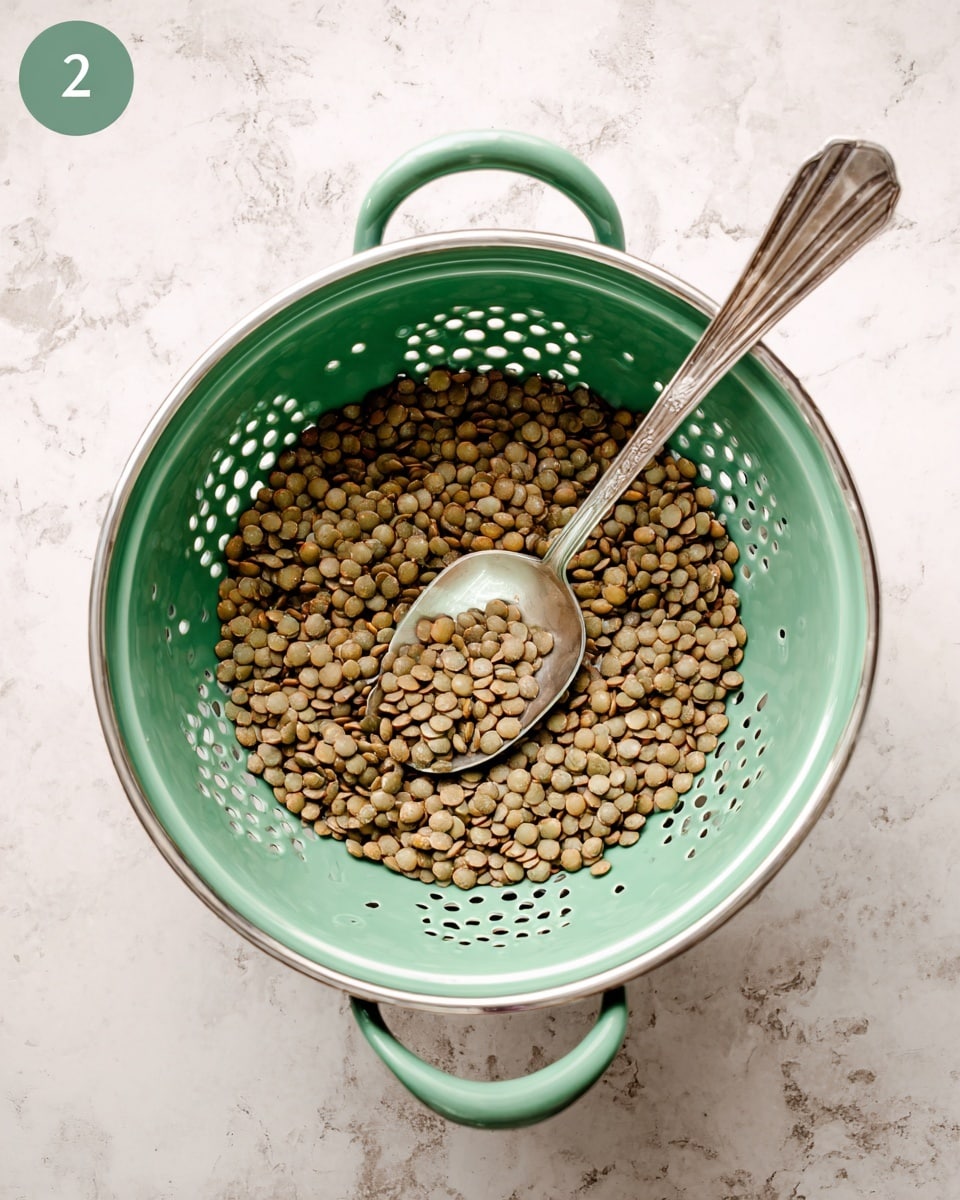 A green colander filled with cooked green lentils, visible through many small holes around its sides, sits on a white marbled surface. Inside the colander, there is a silver spoon resting diagonally with its handle pointing outwards, and some lentils are heaped on the spoon. The colander has two handles on opposite sides. photo taken with an iphone --ar 4:5 --v 7