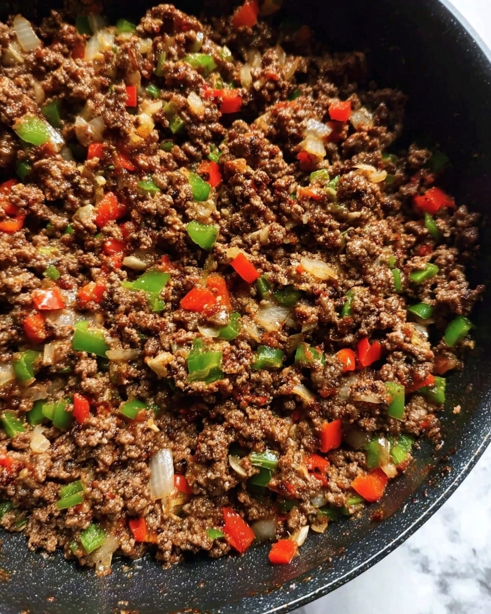 The image shows a black pan filled with cooked ground meat mixed with small chopped pieces of green and red bell peppers and translucent onion pieces. The mixture has a crumbly texture with the vegetables evenly spread throughout the meat. The pan is resting on a surface with a white marbled texture. photo taken with an iphone --ar 4:5 --v 7