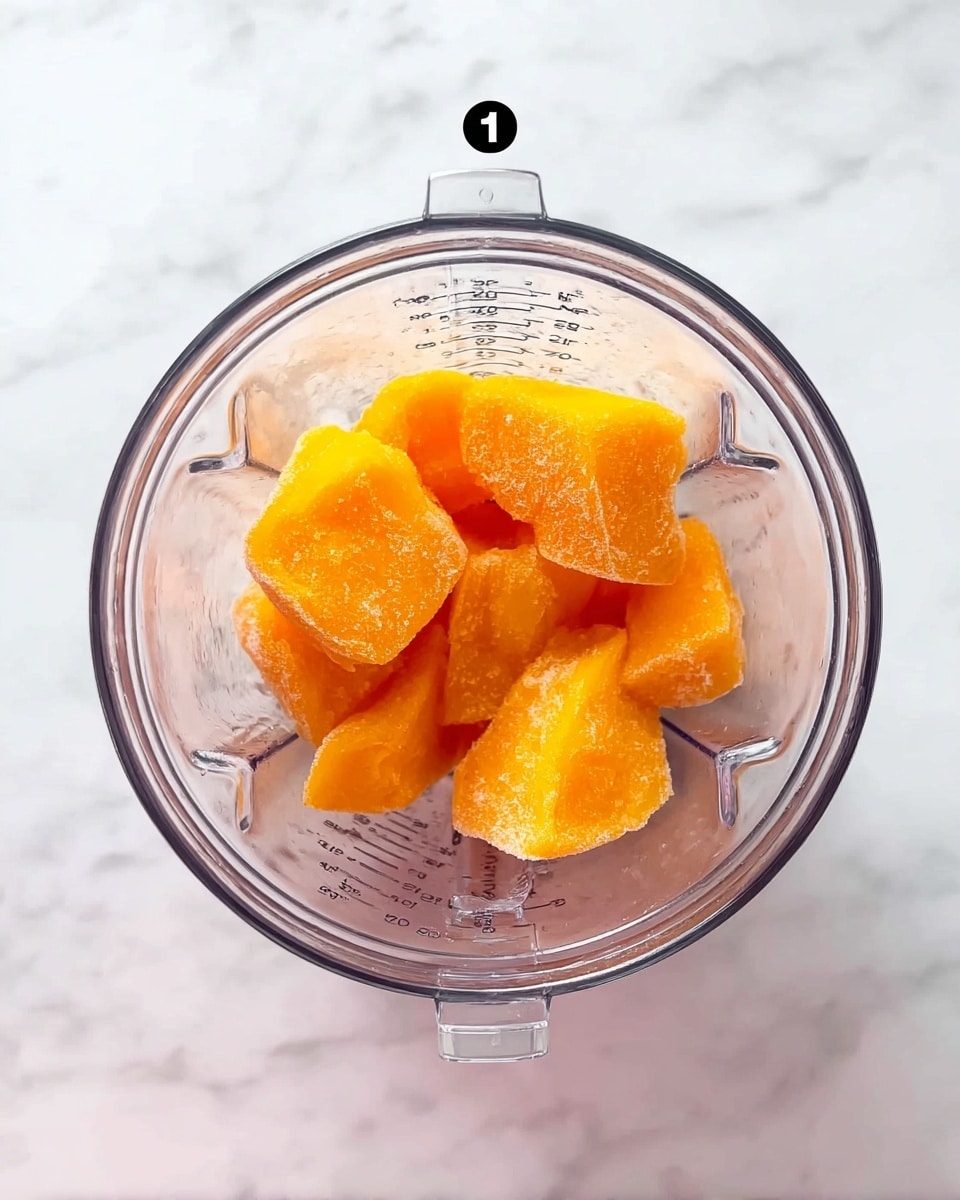 The image shows a top-down view of a clear blender containing several large pieces of bright orange frozen fruit, arranged loosely inside with their frosty texture visible, set against a white marbled surface. The blender jar has measurement markings on the inside. The frozen fruit pieces have a shiny and slightly crystalline look, showing different shapes and sizes. photo taken with an iphone --ar 4:5 --v 7